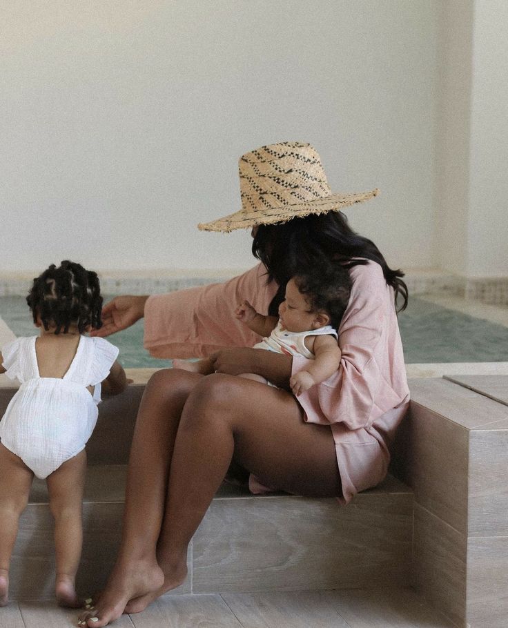 a woman and two small children sitting on a bench in front of a swimming pool