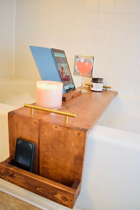 a wooden table with a cell phone and candle on it next to a bathtub