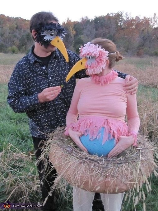 a man standing next to a pregnant woman in a bird costume on top of hay