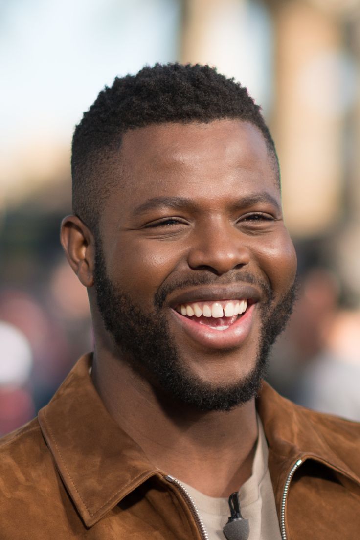 a close up of a person wearing a brown jacket and smiling at the camera with his mouth open