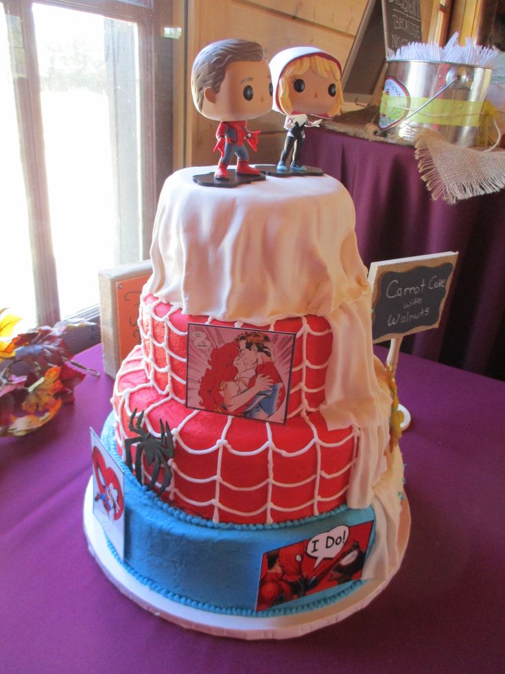 a spiderman themed cake on a purple table cloth with two small figurines