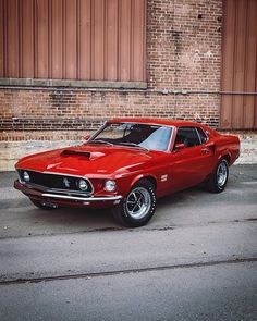 an old red mustang parked in front of a brick building