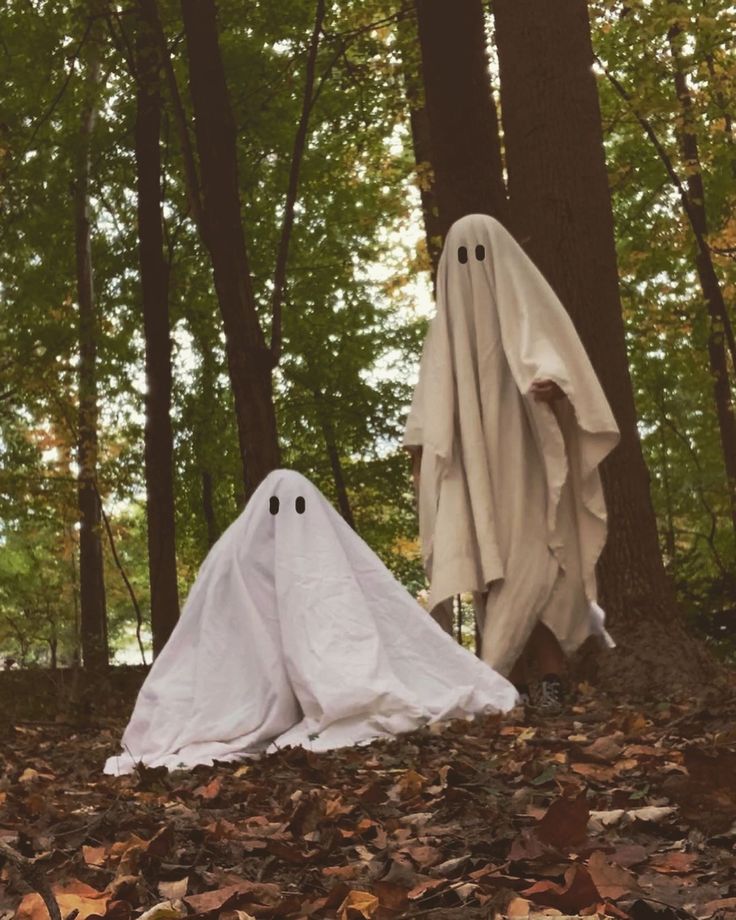 two ghost statues in the woods with leaves on the ground