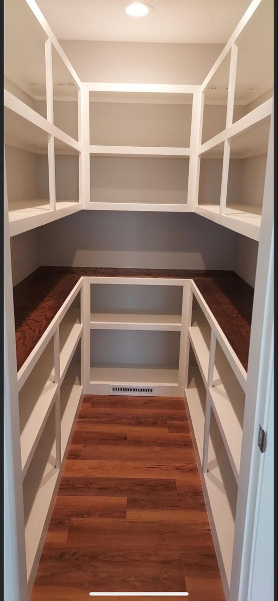 an empty walk - in closet with white shelving and wood flooring is shown