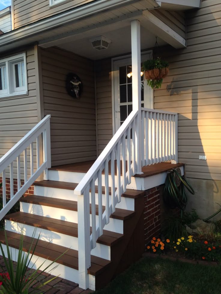 a house with white railings and brown steps leading to the front door on a sunny day