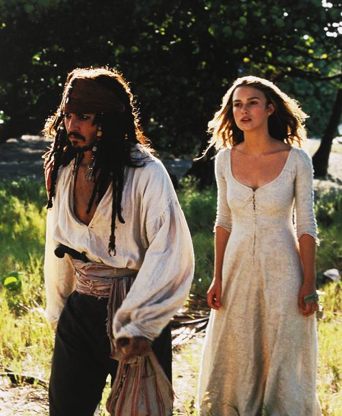 two people dressed up as pirates walking in the grass with one woman wearing a white dress