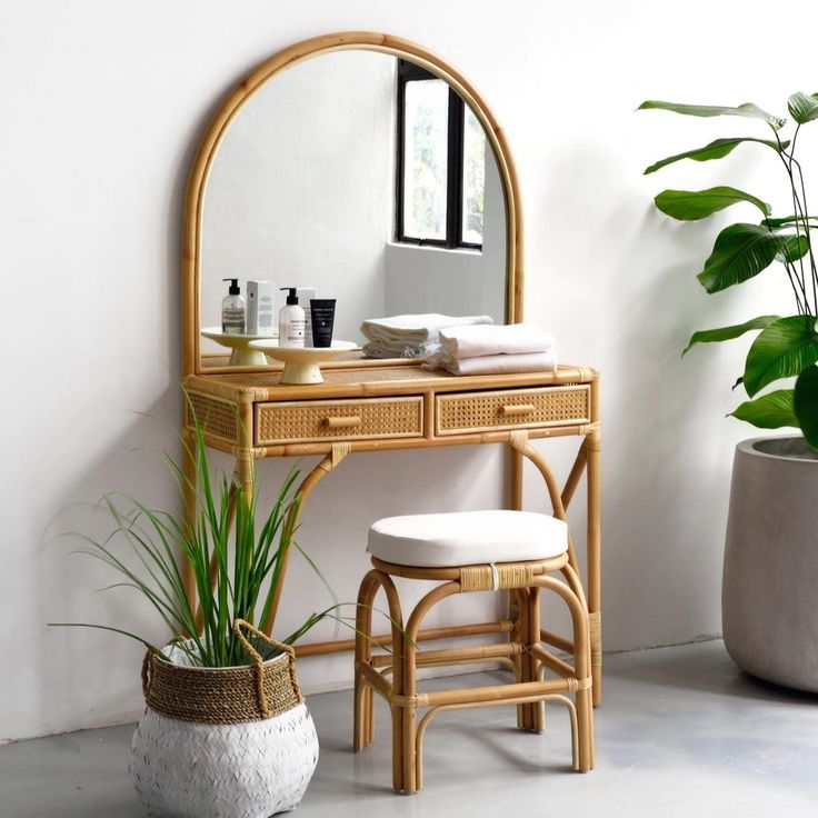 a bamboo vanity with mirror and stool next to potted plant in white walled room