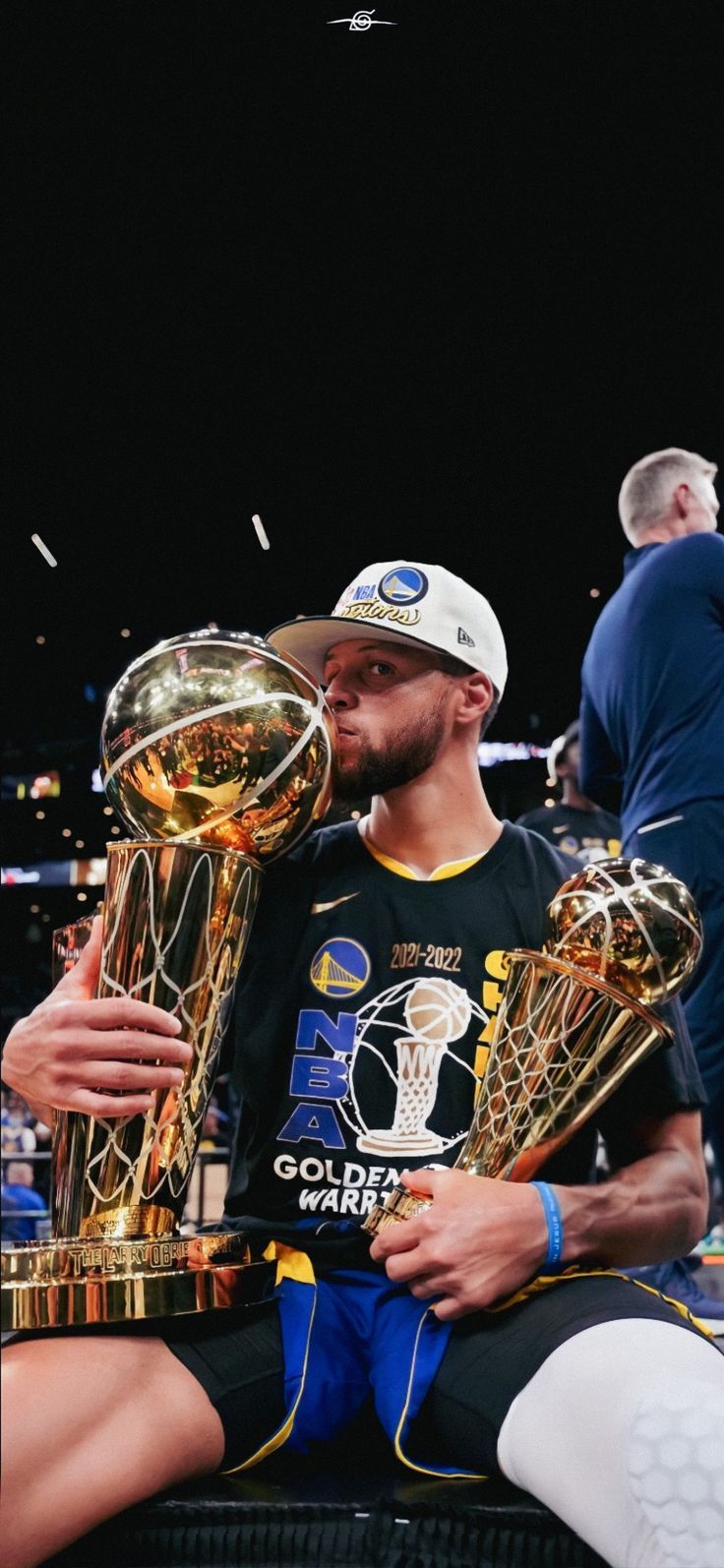 a man sitting on top of a basketball court holding two trophy cups in his hands