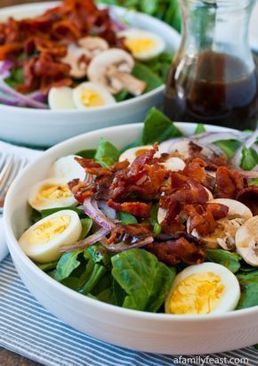 a salad with bacon, hard boiled eggs and spinach leaves in a white bowl