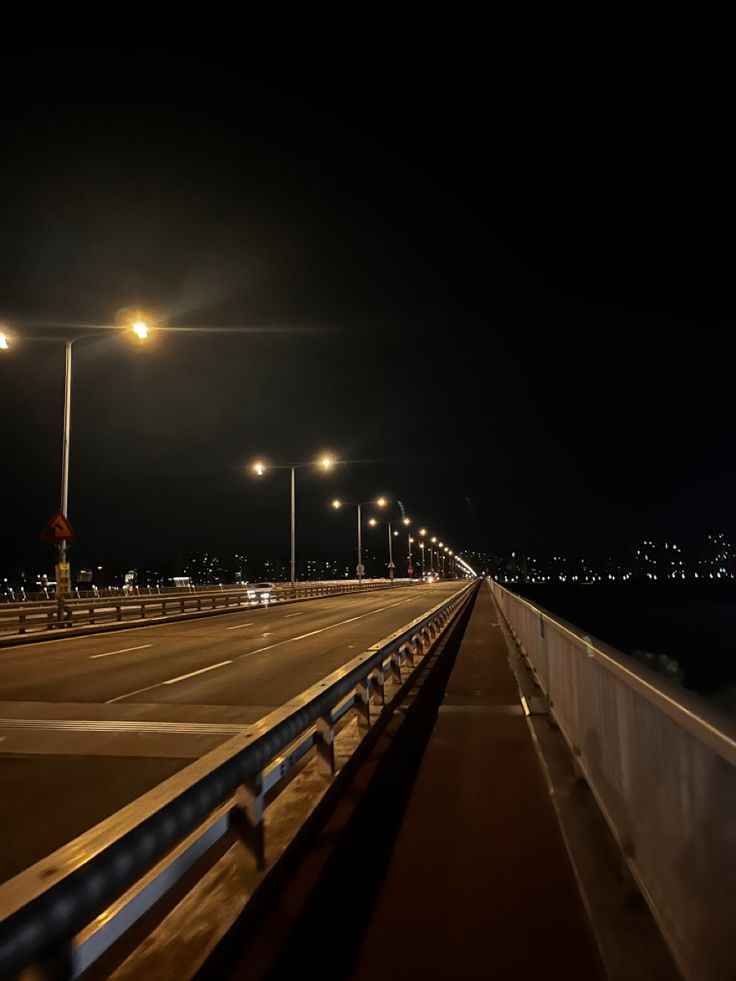 an empty highway at night with street lights and water in the background on a dark, overcast day