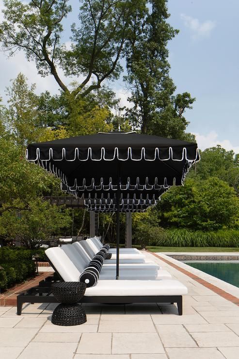 an umbrella and two white couches in front of a swimming pool with trees behind it