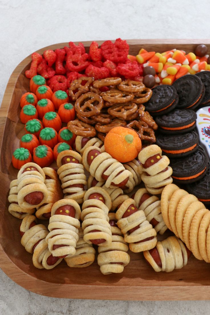 a wooden platter filled with cookies, pretzels, and other treats for halloween