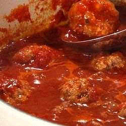 meatballs and tomato sauce in a white bowl with a ladle full of them