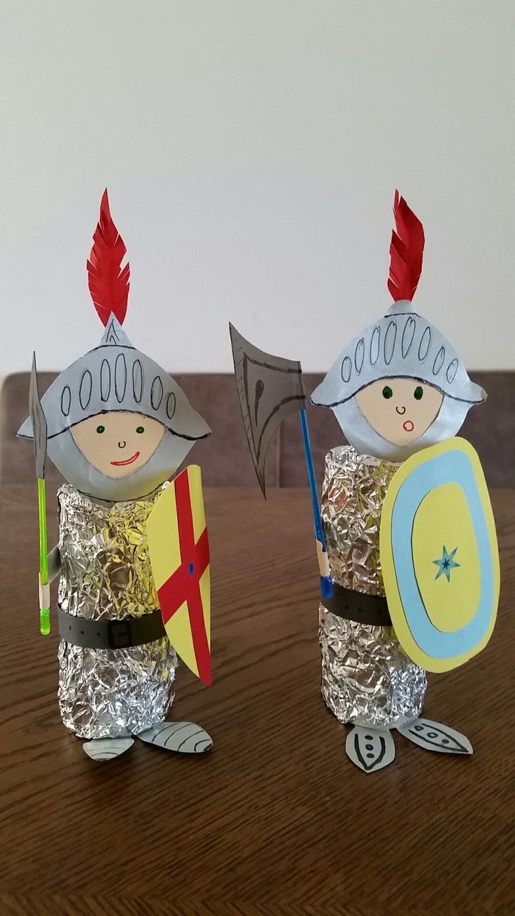 two paper mache knights holding shields and shield on a wooden table next to each other