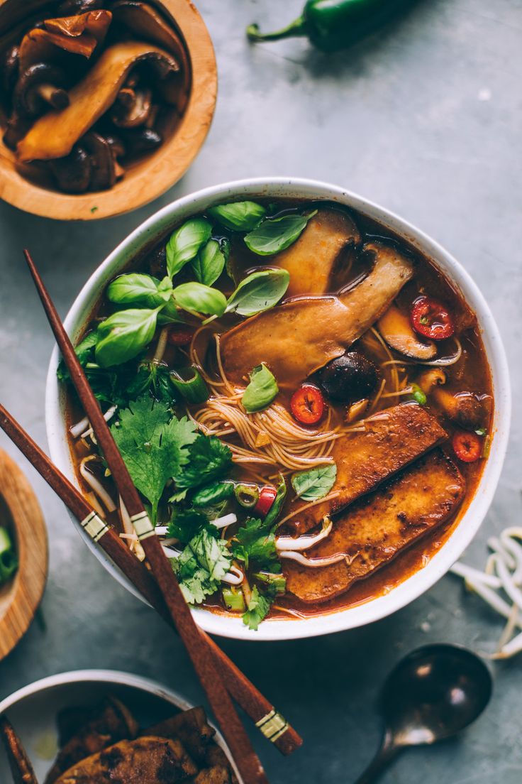 two bowls of soup with chopsticks and spoons next to them on a table