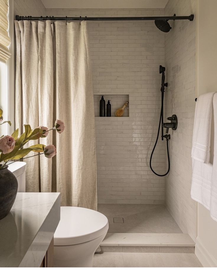 a bathroom with a shower, toilet and sink in it's center area next to a window