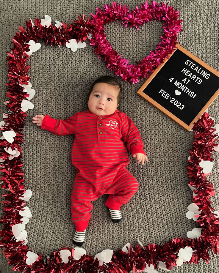 a baby is laying in a heart shaped frame with tinsel on the floor next to it