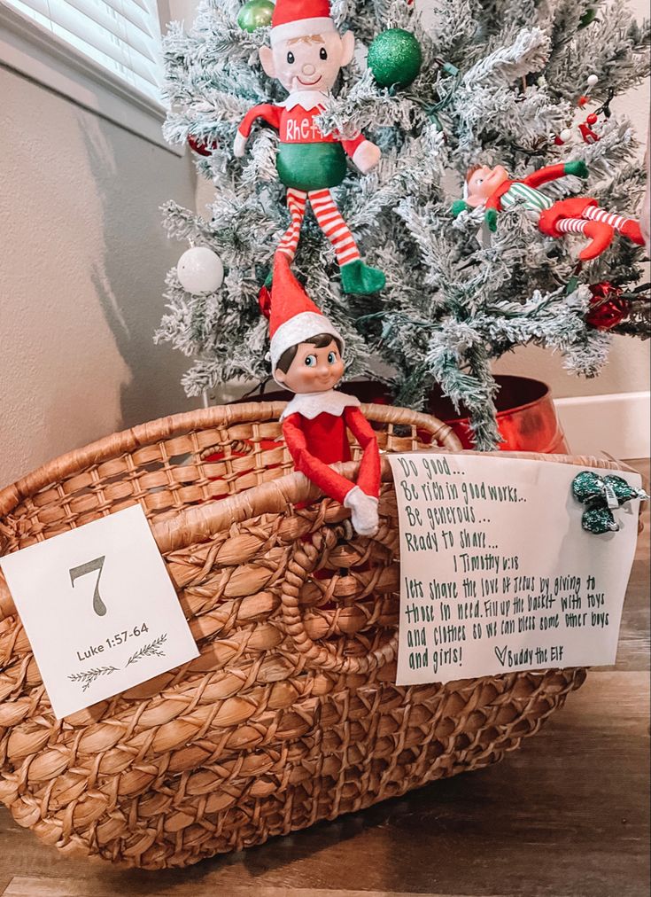 an elf is sitting in a basket next to a christmas tree with notes on it