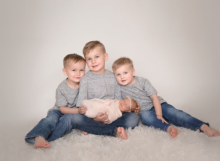 three little boys sitting on top of each other while holding a baby in their arms