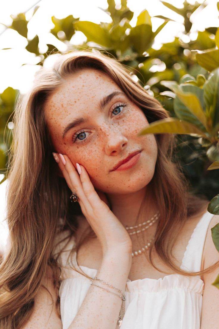 a woman with freckles on her face posing for a photo in front of some leaves