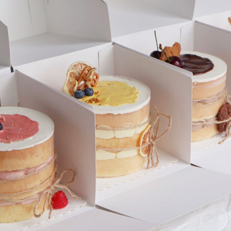 three cakes in boxes with different toppings on each side and one is decorated with berries