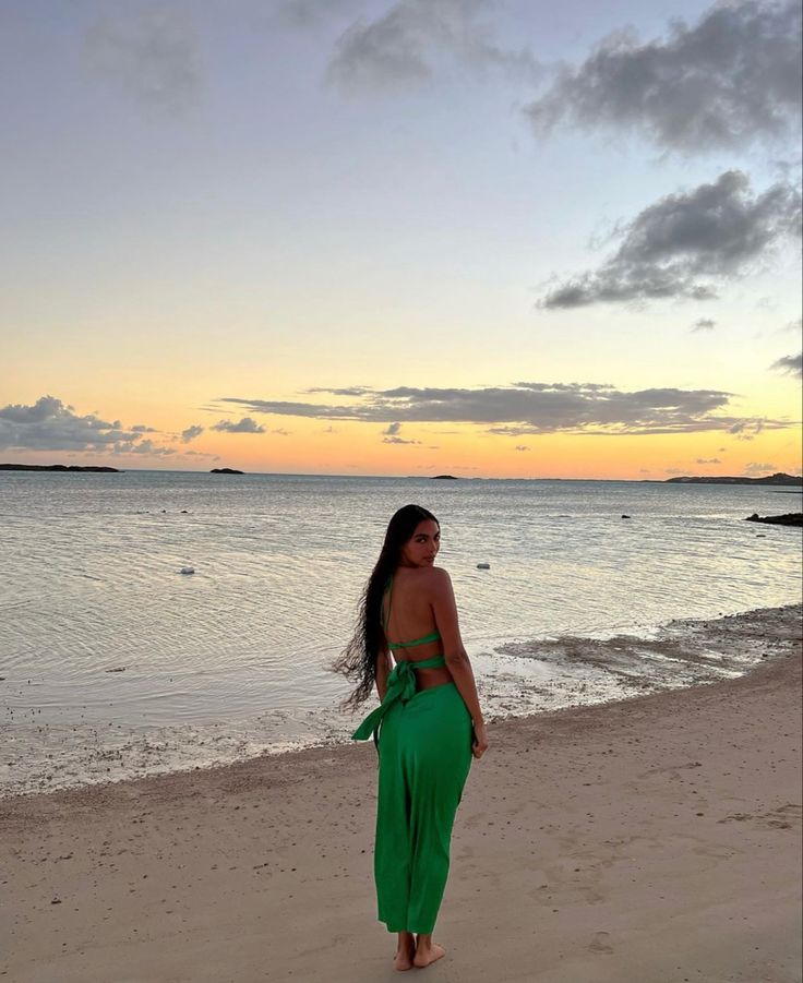 a woman standing on top of a sandy beach next to the ocean in a green dress