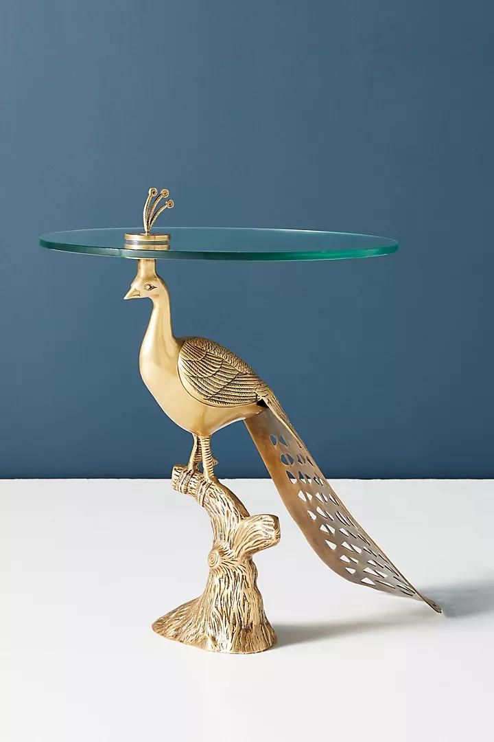 a glass table with a gold bird on it's base and a blue wall in the background