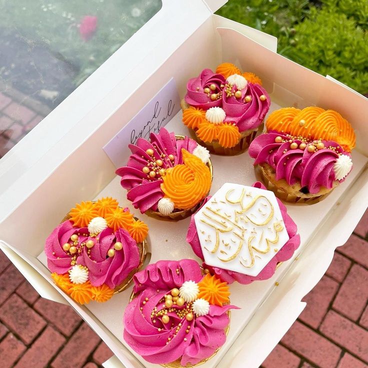 six cupcakes with pink and orange frosting in a box on a table