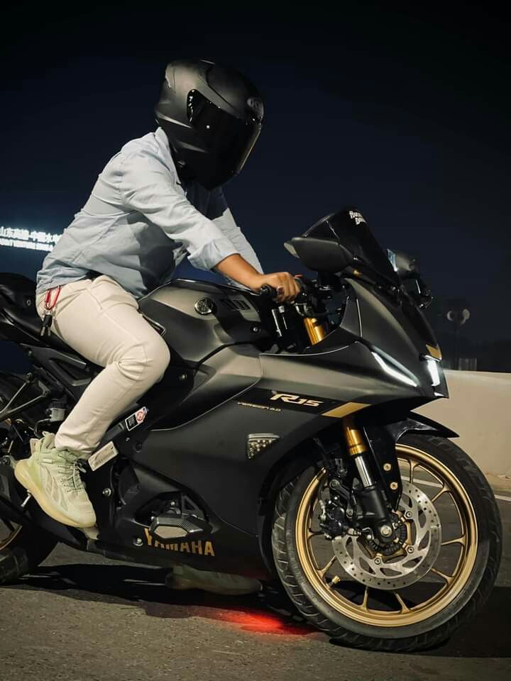 a person riding on the back of a black motorcycle at night with its lights on