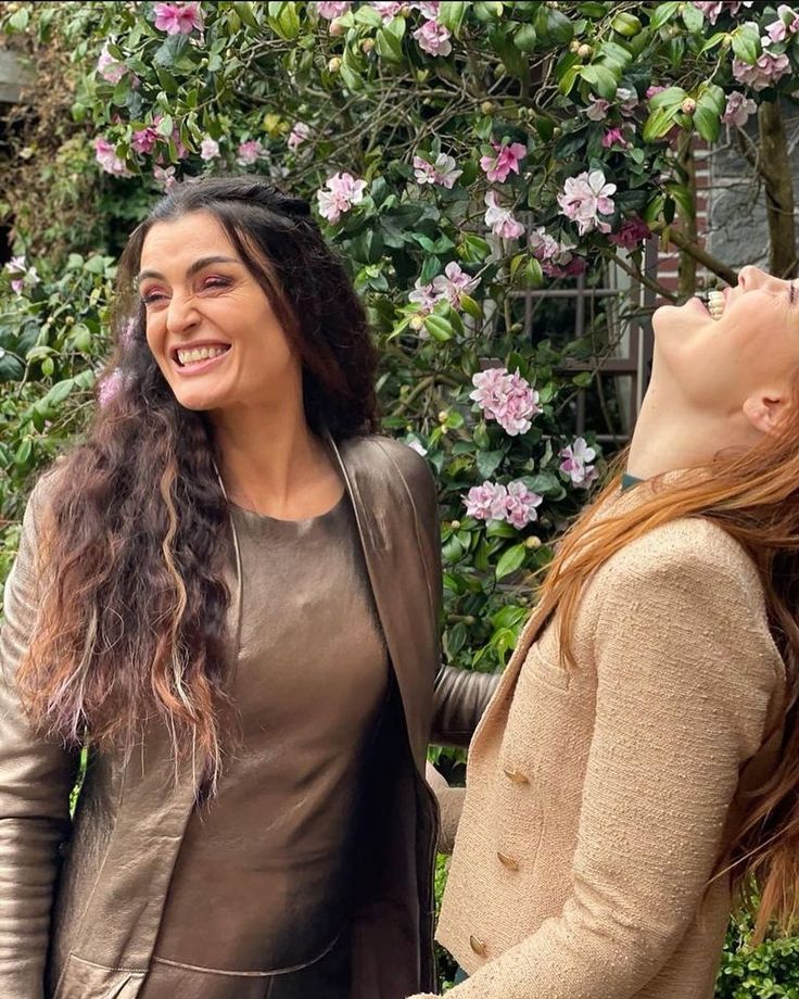 two women standing next to each other in front of flowers