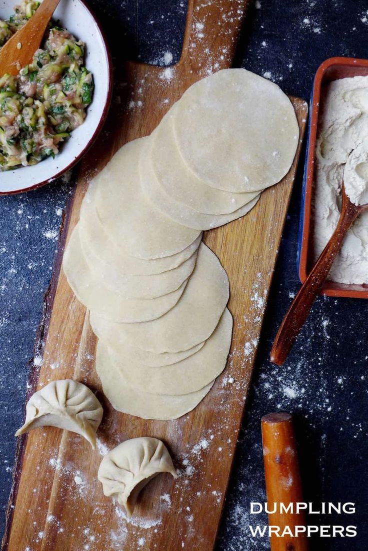 some dumplings are sitting on a cutting board next to bowls and utensils