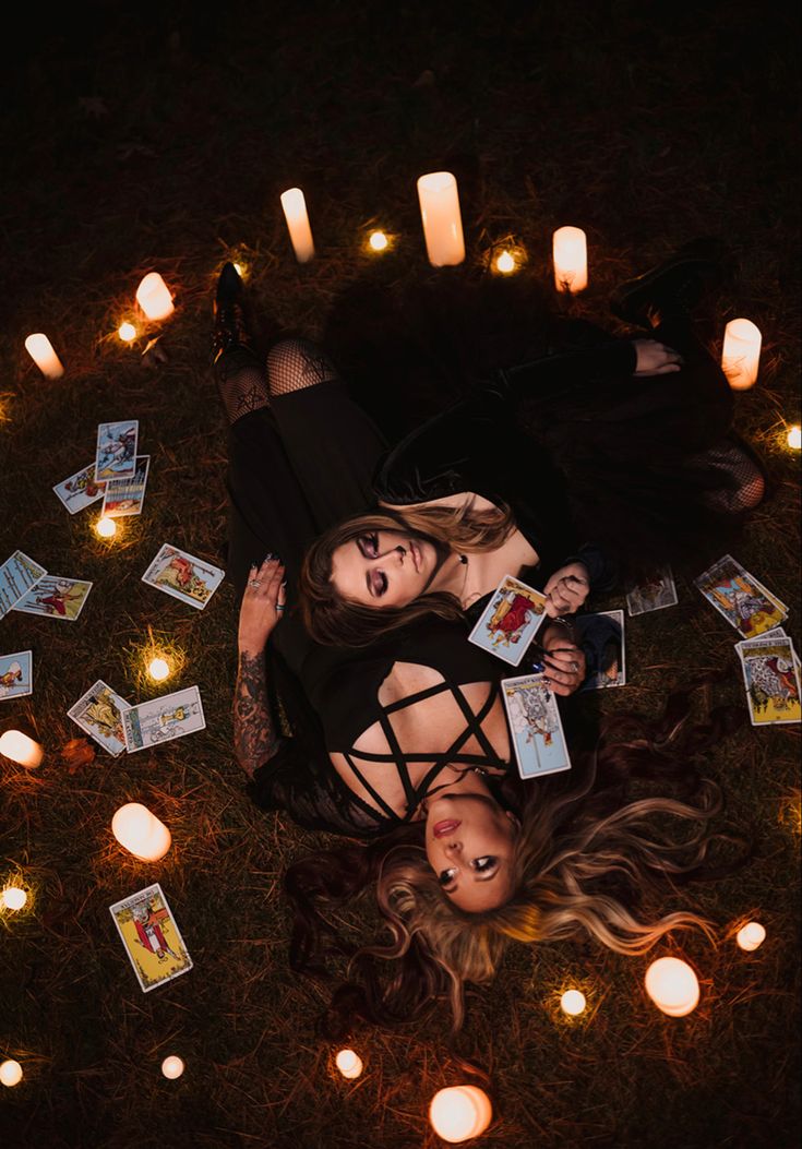 two women are laying on the ground surrounded by candles and playing cards with each other