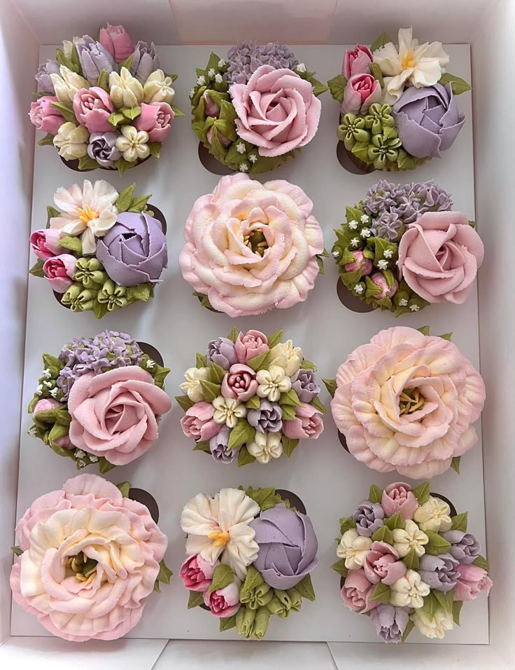 cupcakes decorated with pink and purple flowers in a white box on a table