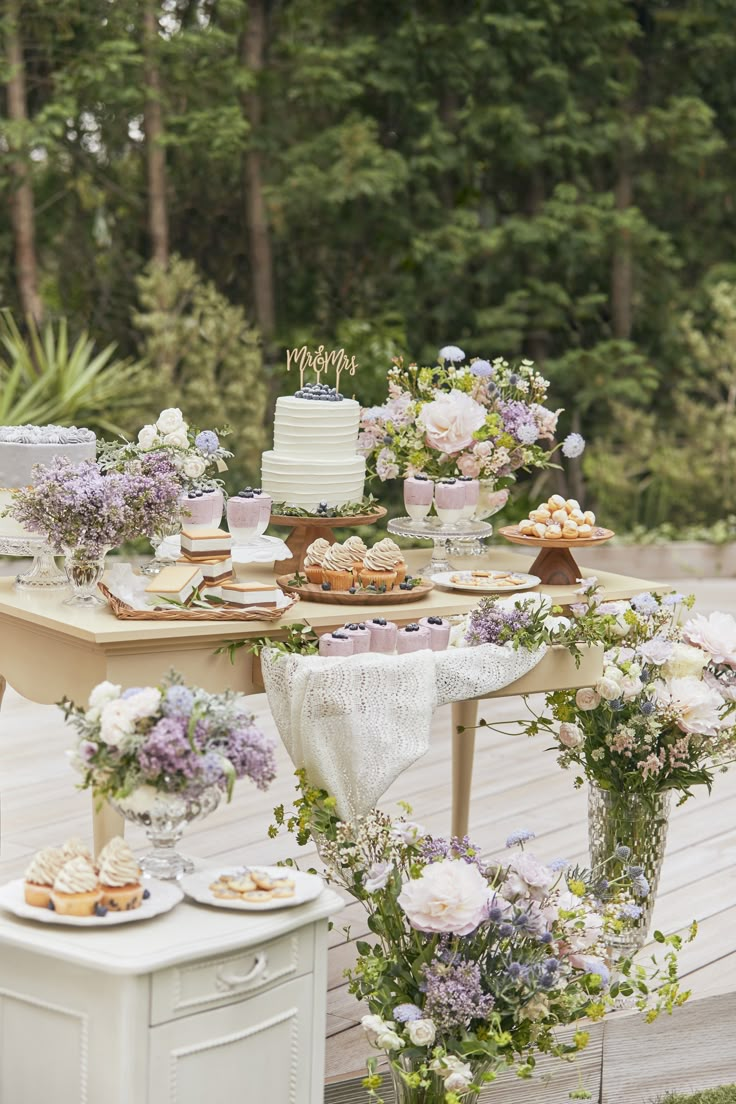 a table topped with cakes and desserts on top of a wooden floor covered in greenery