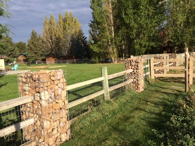 the fence is made out of wood and has stone blocks on it, along with green grass