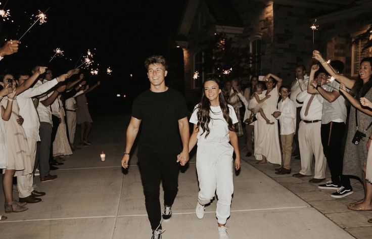 a man and woman walking down the street with sparklers in their hands as people look on