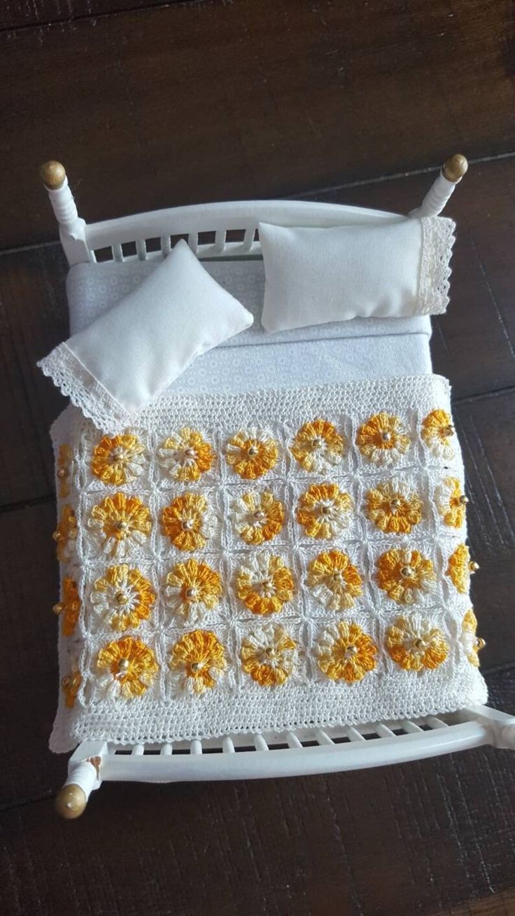 a crocheted bed with white and yellow flowers on the bottom, along with two pillows