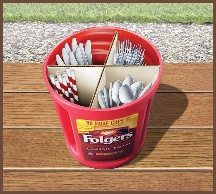 a red bucket filled with silverware on top of a wooden table next to grass