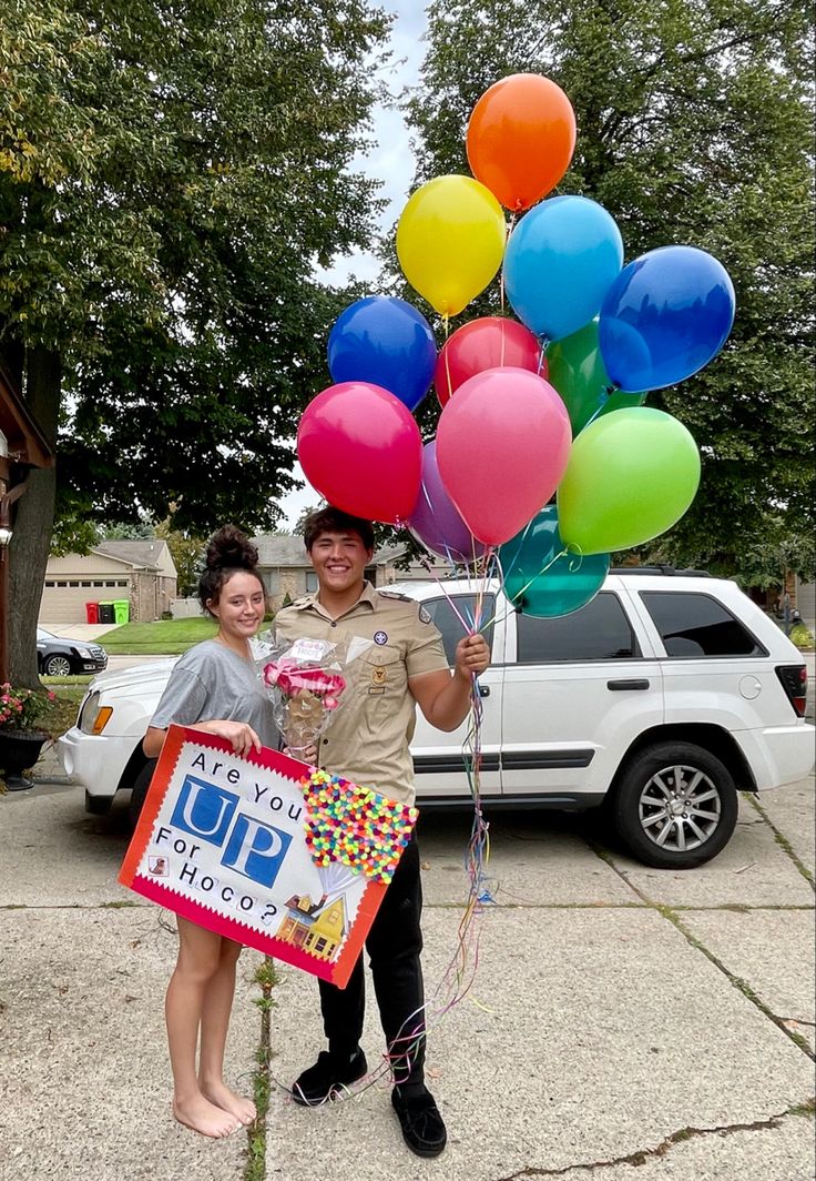 a man and woman holding up balloons in front of a car with a sign on it