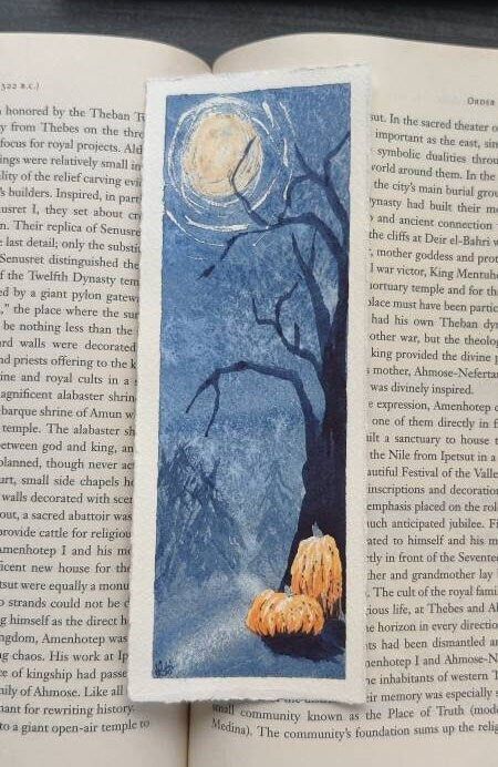 an open book with a picture of a tree in the middle and a full moon above it