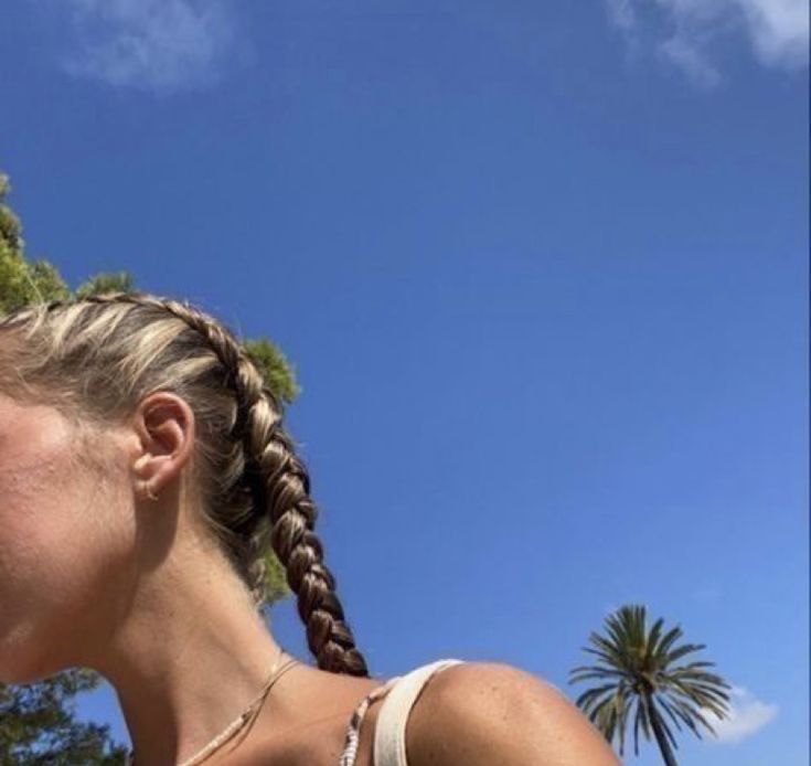 a woman with braids on her hair standing in front of palm trees and blue sky