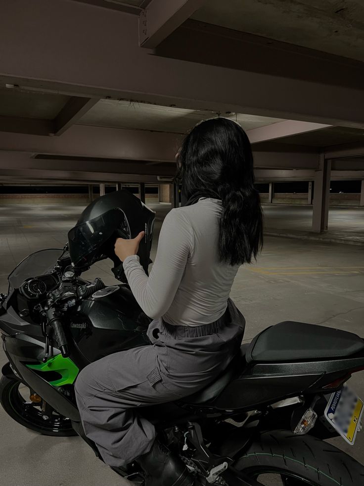 a woman riding on the back of a black motorcycle in a parking lot at night