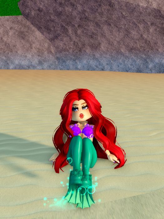 a little mermaid sitting on top of a sandy beach