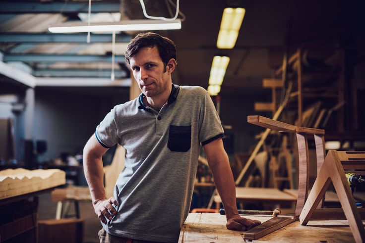 a man standing next to a wooden chair in a room filled with woodworking equipment