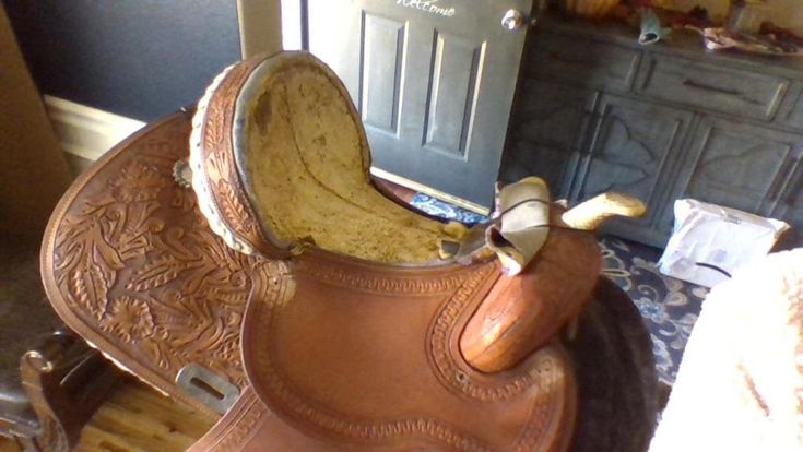 a brown horse saddle sitting on top of a wooden floor next to a black door