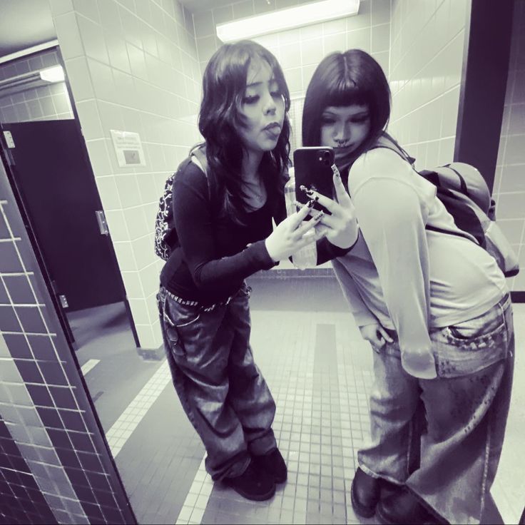 two women standing in a bathroom looking at their cell phones