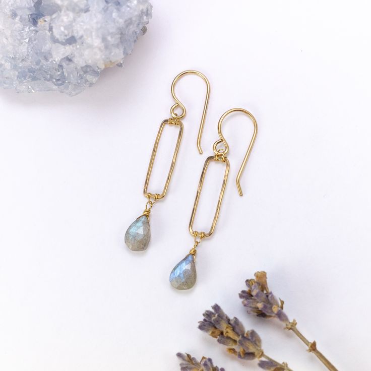 two pairs of earrings sitting next to each other on top of a rock and lavender flowers