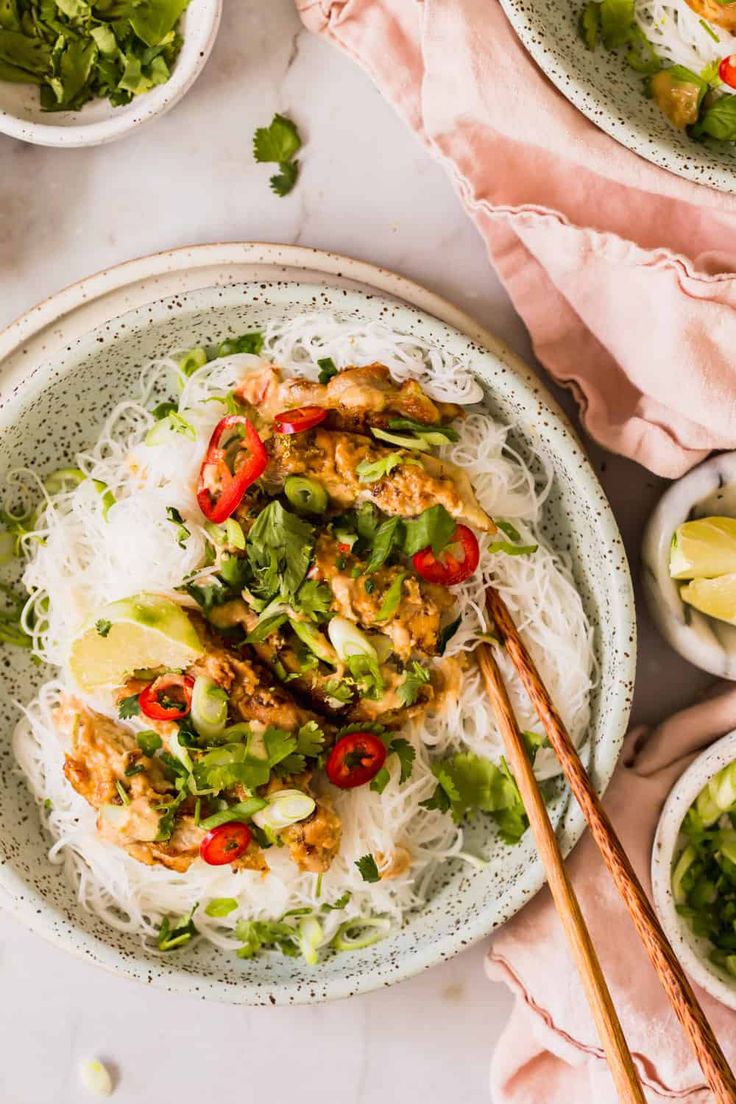 two plates with chicken and rice on them next to chopsticks, lemon wedges and cilantro