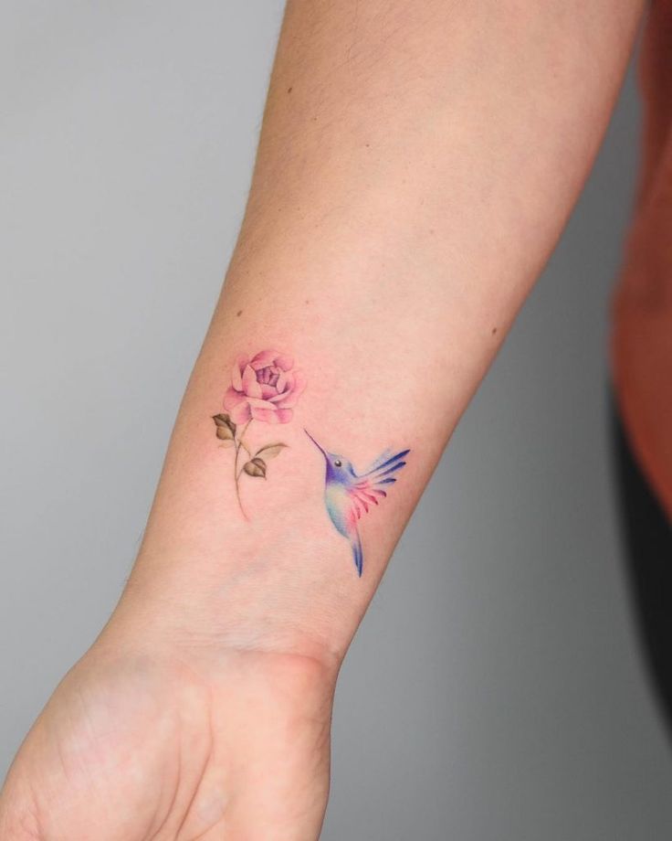 a small tattoo on the wrist of a woman with a hummingbird and pink rose