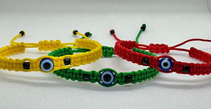 three bracelets with evil eyes are on a white tablecloth and one is red, the other is green